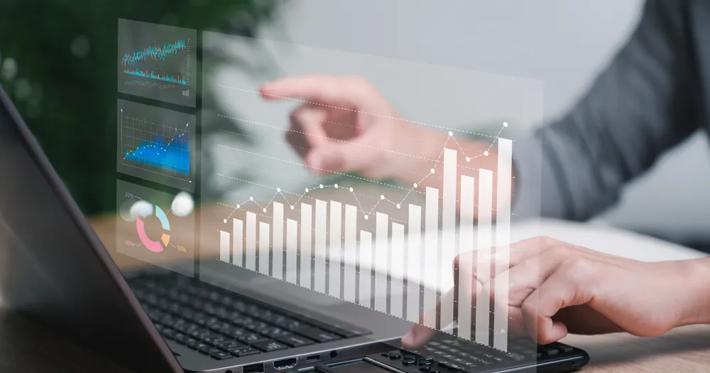 Hand pointing at a laptop with floating analytics charts and graphs above the keyboard
