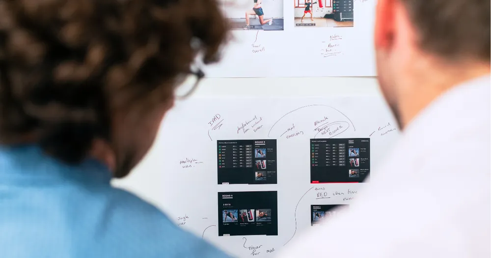 Two people reviewing a whiteboard covered in website wireframe sketches and layouts
